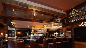 Zona de bar con varios taburetes, una barra y una variedad de botellas y vasos.