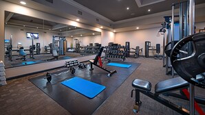 Un gimnasio con equipo de ejercicio, colchonetas azules y un espejo grande.