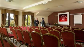 A conference room with rows of red chairs, a podium, and a projector screen displaying 'Kilmurry Lodge Hotel'.