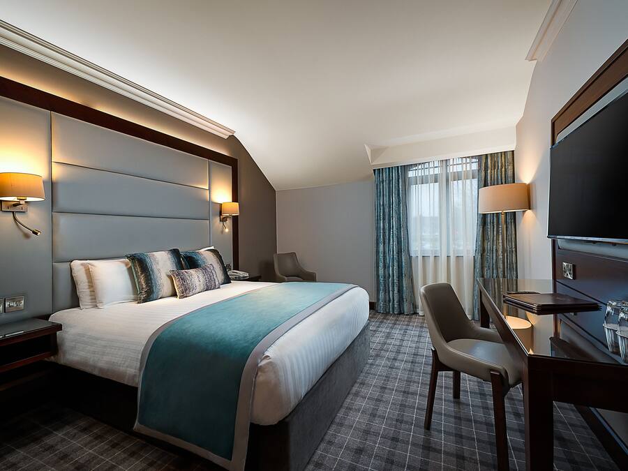 A hotel room with a large bed, a desk with a chair, a television, and a window with curtains.