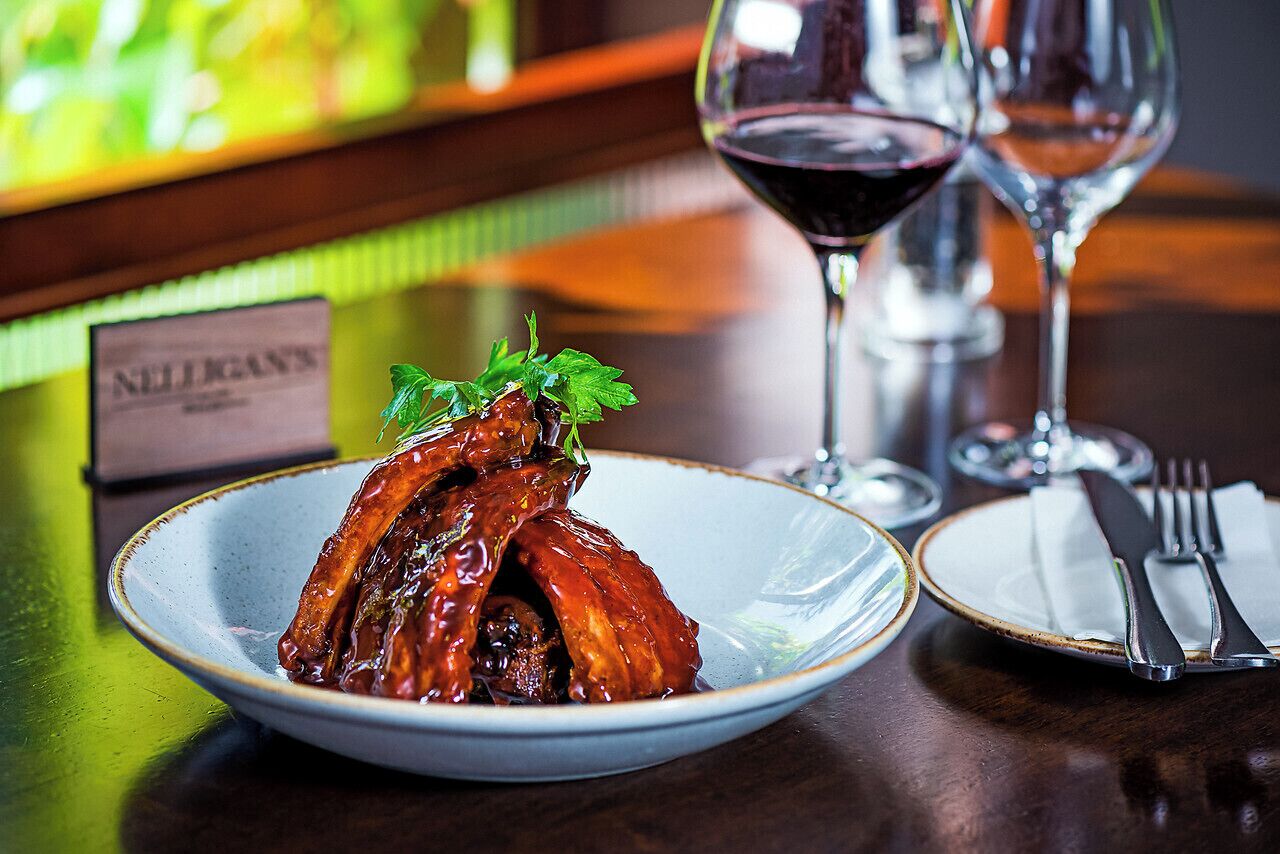 A plate of glazed chicken wings with a garnish, a wine glass, and a menu sign on a table.