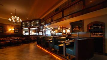 Un restaurante con suelos de madera, asientos tapizados en verde y una zona de bar con estantes llenos de botellas.