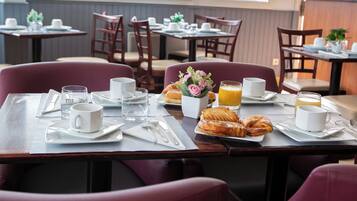 A breakfast setting with a table set for two, including croissants, orange juice, and coffee.