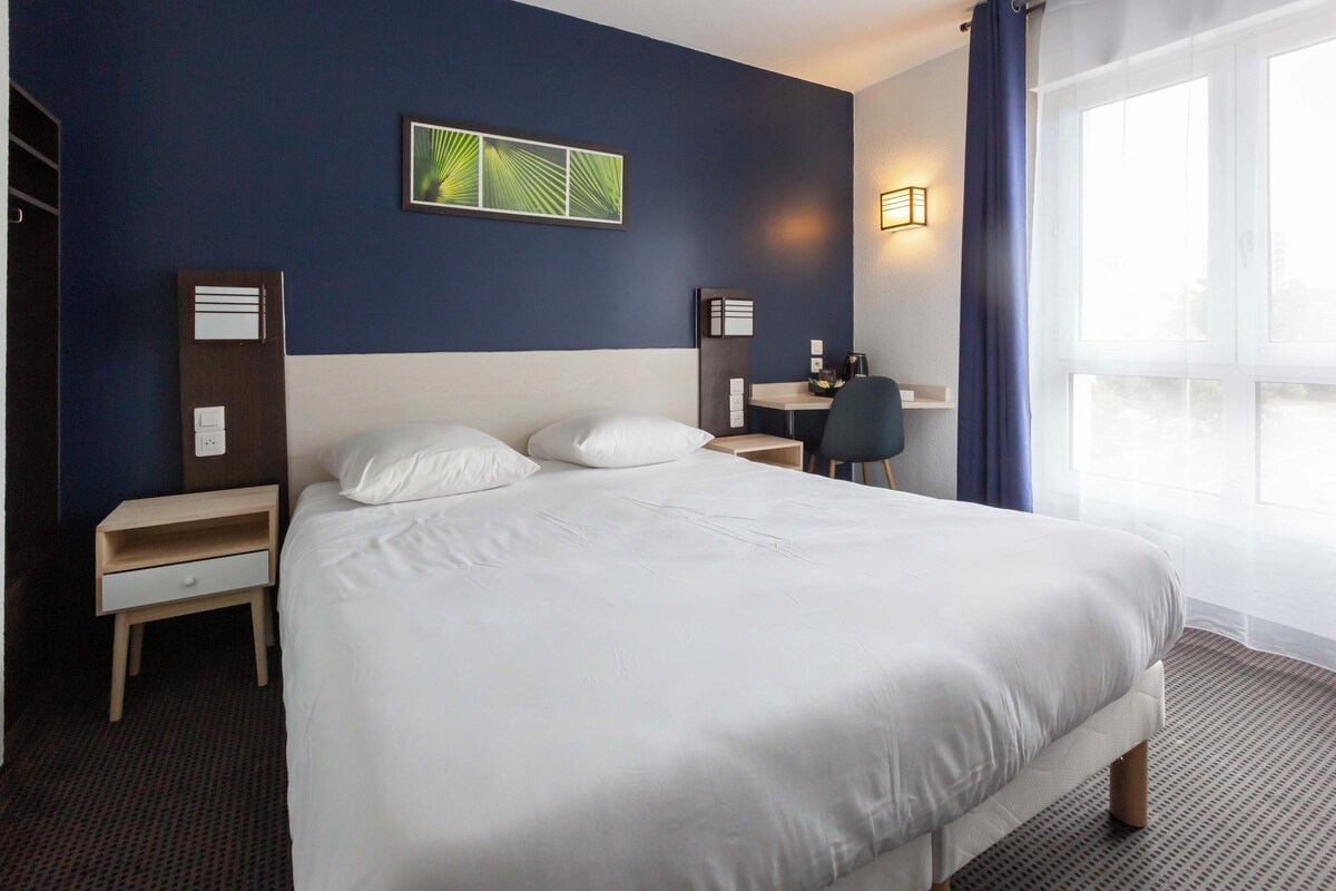 A hotel room with a large bed, bedside tables, a desk, and a chair.