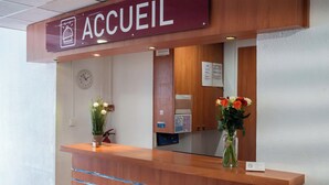 A reception desk with a clock, a sign reading "ACCUEL", and two vases with flowers.