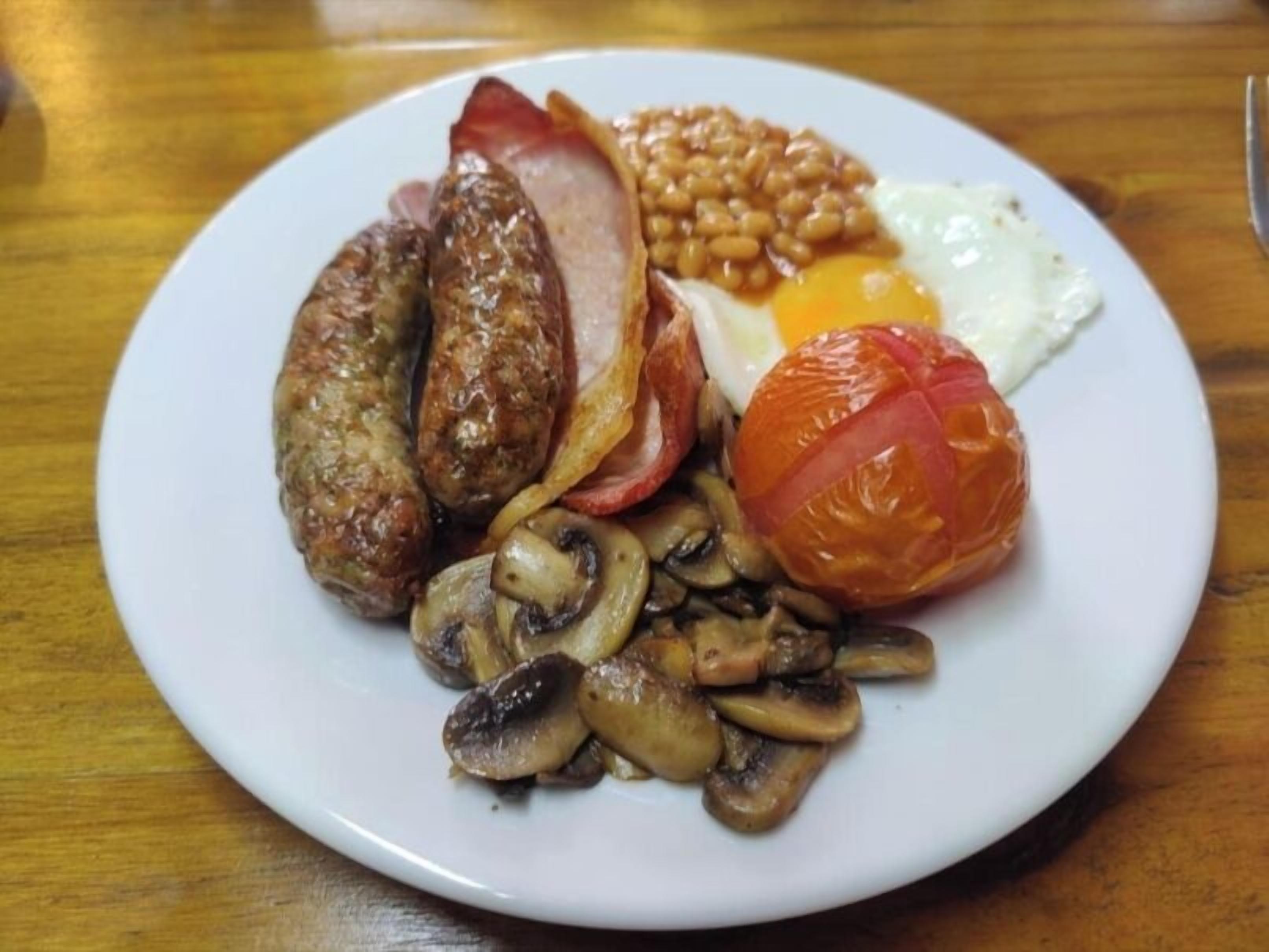 A plate of breakfast food including sausages, bacon, eggs, beans, mushrooms, and a tomato.