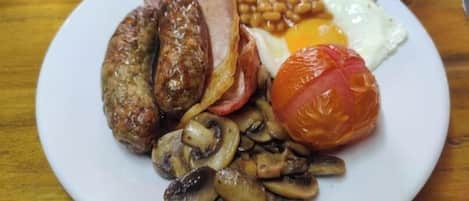 A plate of breakfast food including sausages, bacon, eggs, beans, mushrooms, and a tomato.
