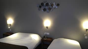 A hotel room with two beds, each with a white comforter and a dark throw blanket. There are wall-mounted lamps on either side of the beds, and a decorative wall piece above the beds.