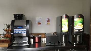 A self-service coffee station with a digital menu display, a red electric kettle, and two beverage dispensers.