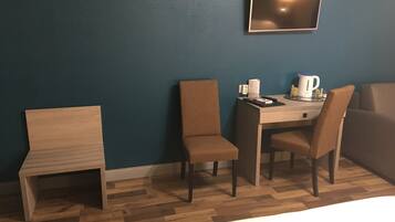 Quarto de hotel com uma cama, uma escrivaninha com duas cadeiras, uma cafeteira e uma televisão de tela plana na parede.