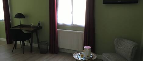 A room with a bed, a desk, a chair, a table with a kettle, and a TV on the wall.