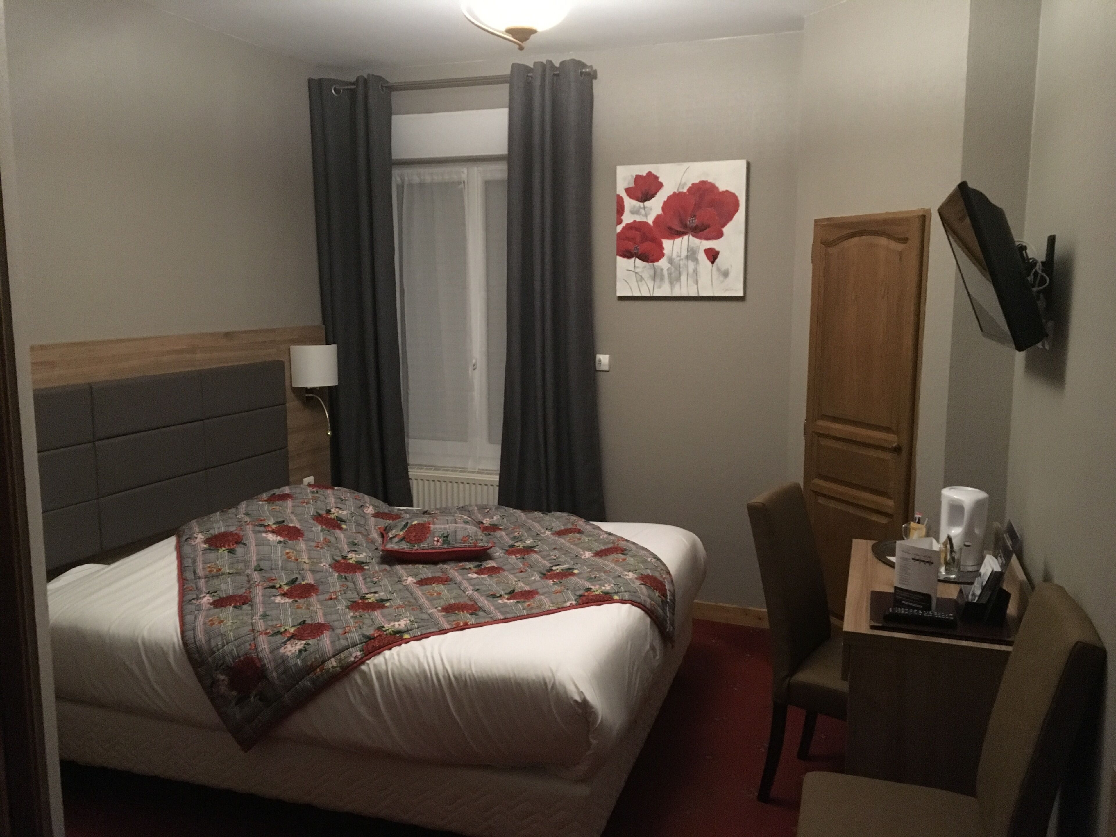 A hotel room with a bed, a desk, a chair, a TV, and a painting on the wall.