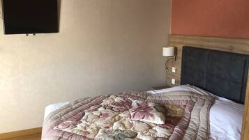 A bedroom with a bed, a television mounted on the wall, a bedside lamp, and a wooden headboard.