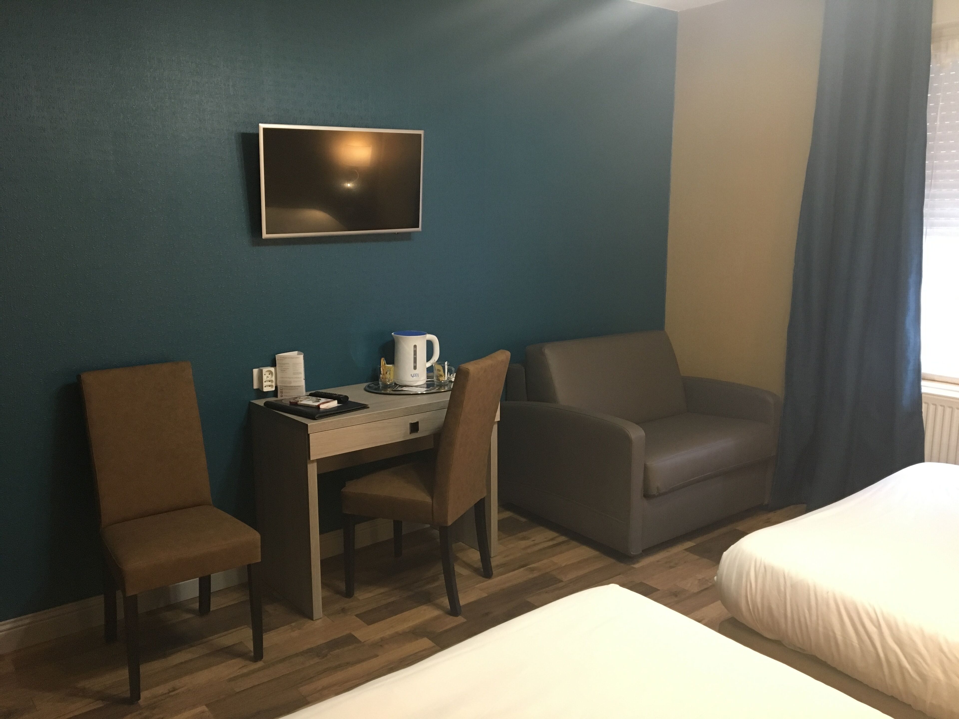 Habitación de hotel con escritorio, dos sillas, cama y televisor montado en la pared.