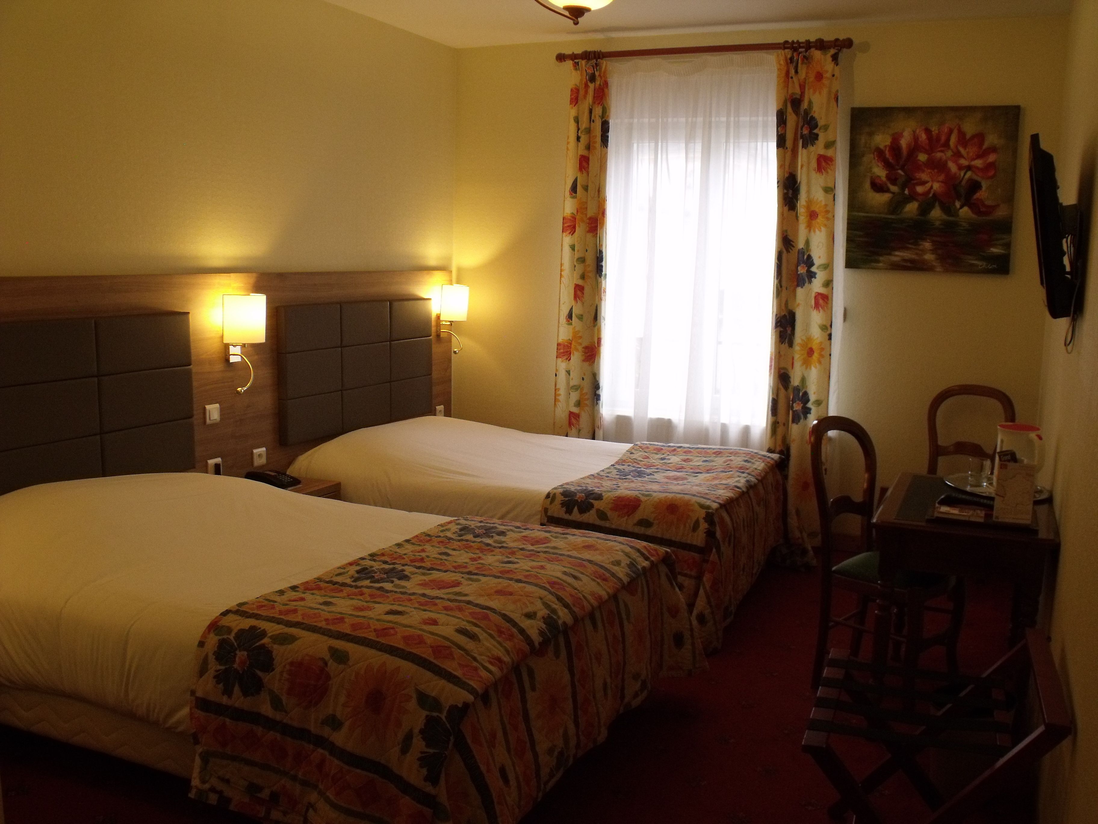 Hotellihuone, jossa on kaksi sänkyä, työpöytä ja tuoli.