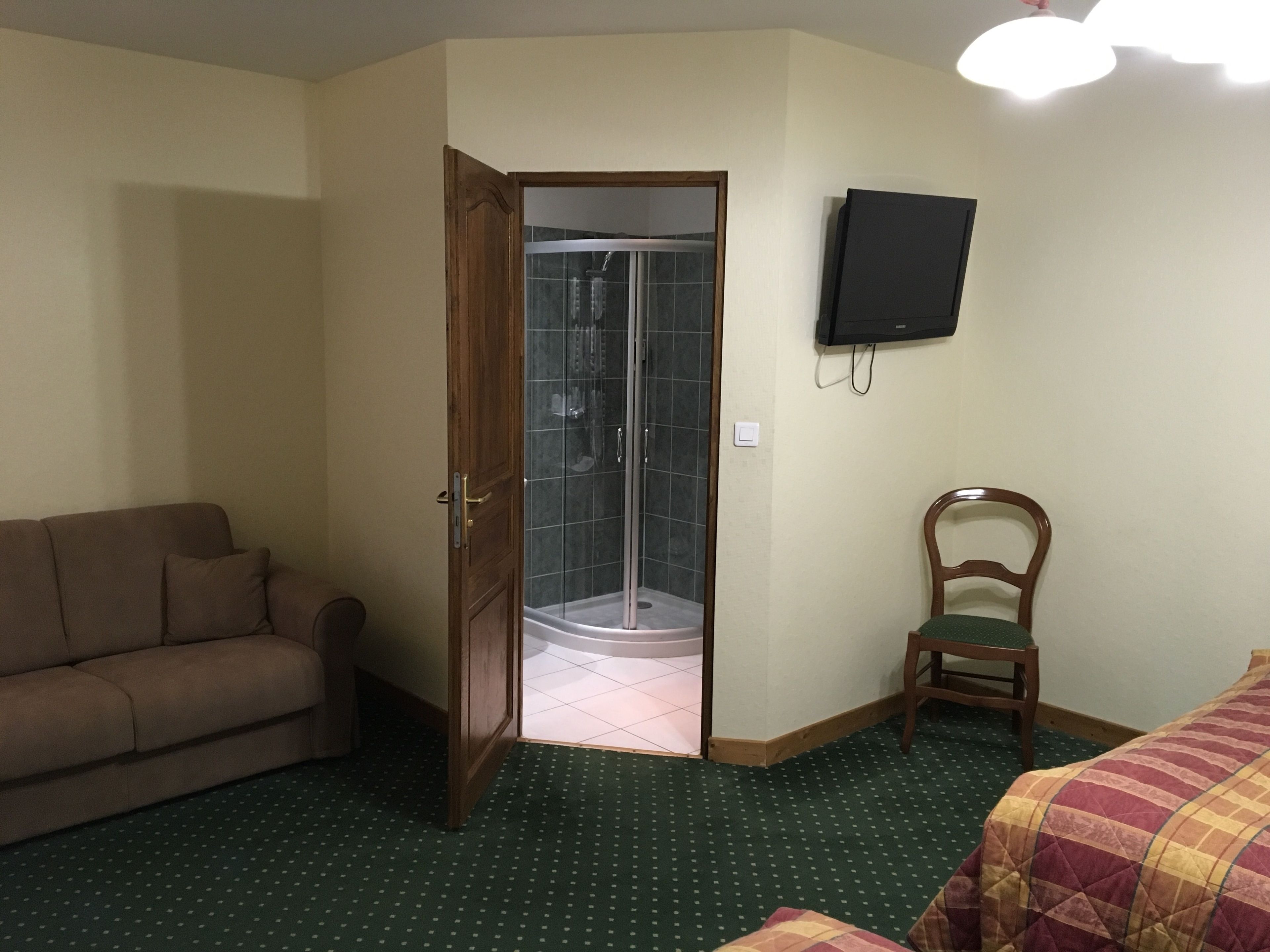 A room with a shower, a television, a couch, and a chair.