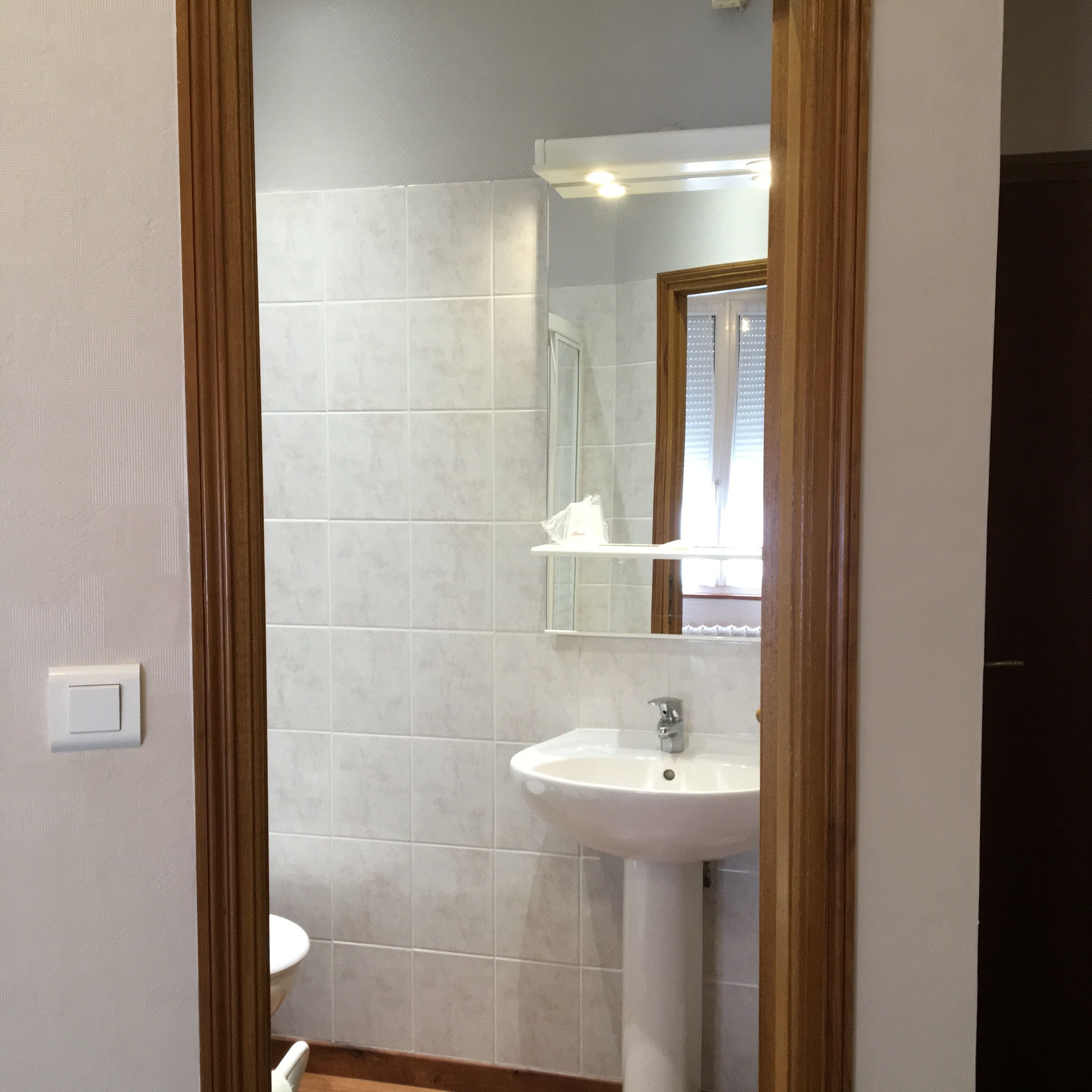 Un baño con lavamanos blanco, espejo y retrete.