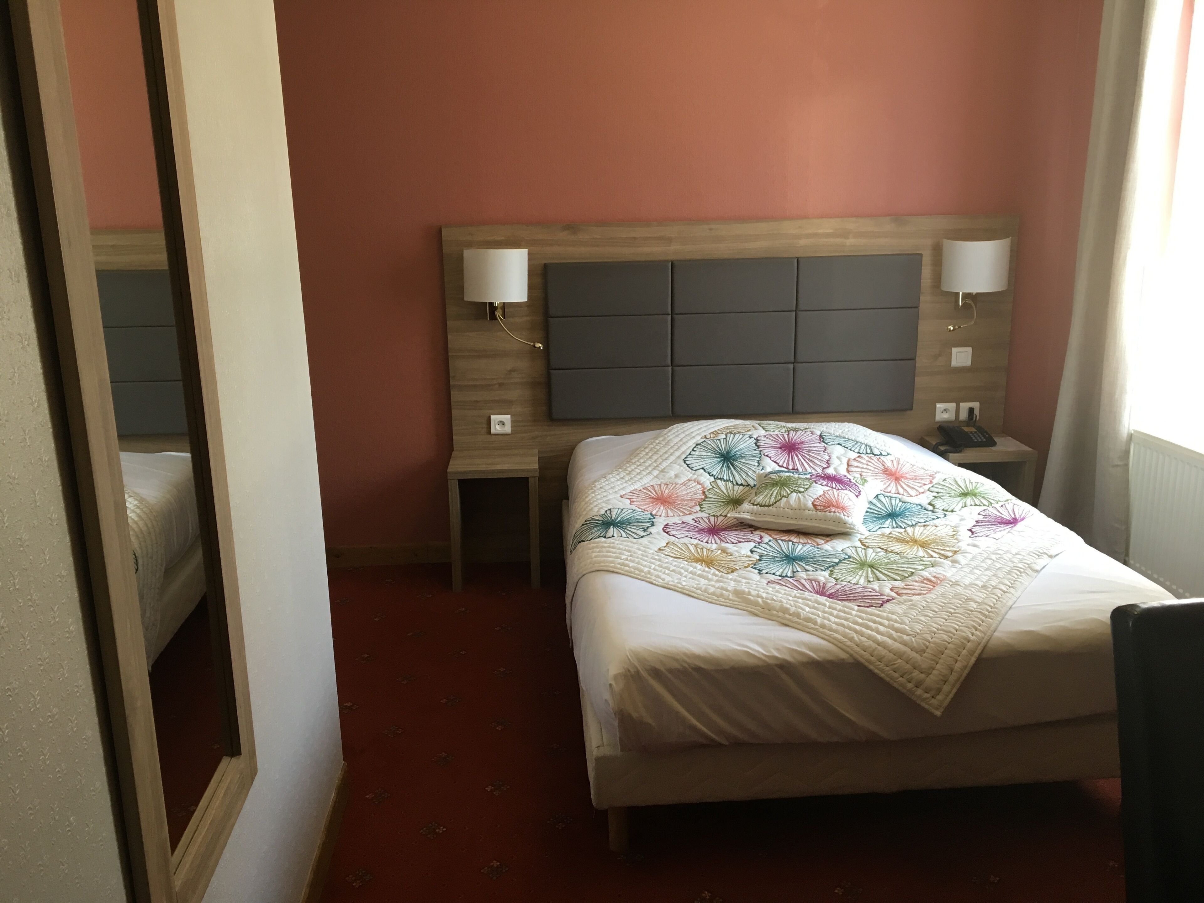 Ett hotellrum med en säng, två sängbord, en spegel och ett fönster.