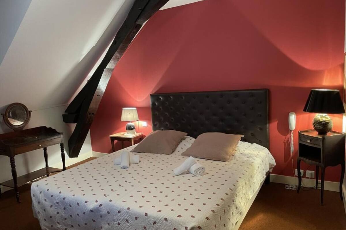 A bedroom with a sloped ceiling, a bed with a headboard, bedside tables, a lamp, and a wall-mounted telephone.