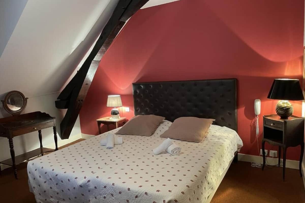 Ein Schlafzimmer mit schrägen Wänden, einem Bett mit Kopfteil, Nachttischen, einer Lampe und einem an der Wand befestigten Telefon.