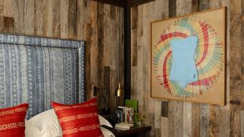 Uma cama com almofadas brancas e vermelhas, uma cabeceira de madeira e uma obra de arte emoldurada na parede.