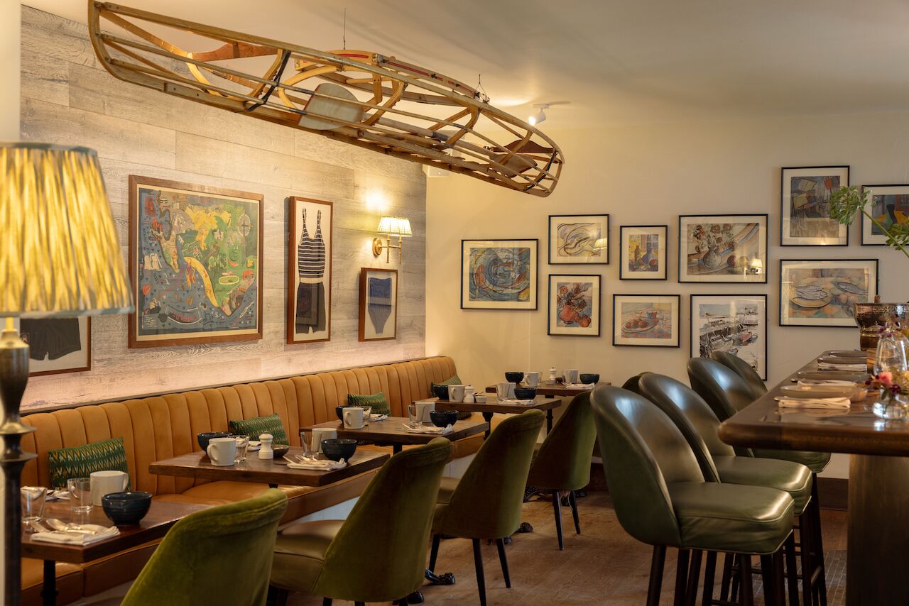 Un restaurante con estructura de techo de madera, una zona de asientos en banco y varias obras de arte enmarcadas en las paredes.