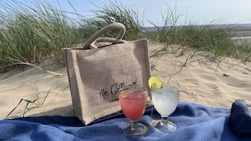 Une scène de plage avec un sac en toile de jute étiqueté « The Go.Mart » et deux boissons posées sur une serviette bleue.