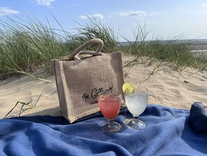 Eine Strandansicht mit einer Jute-Tasche mit dem Aufdruck 'the Go.Mart' und zwei Getränken auf einer blauen Handtuch.