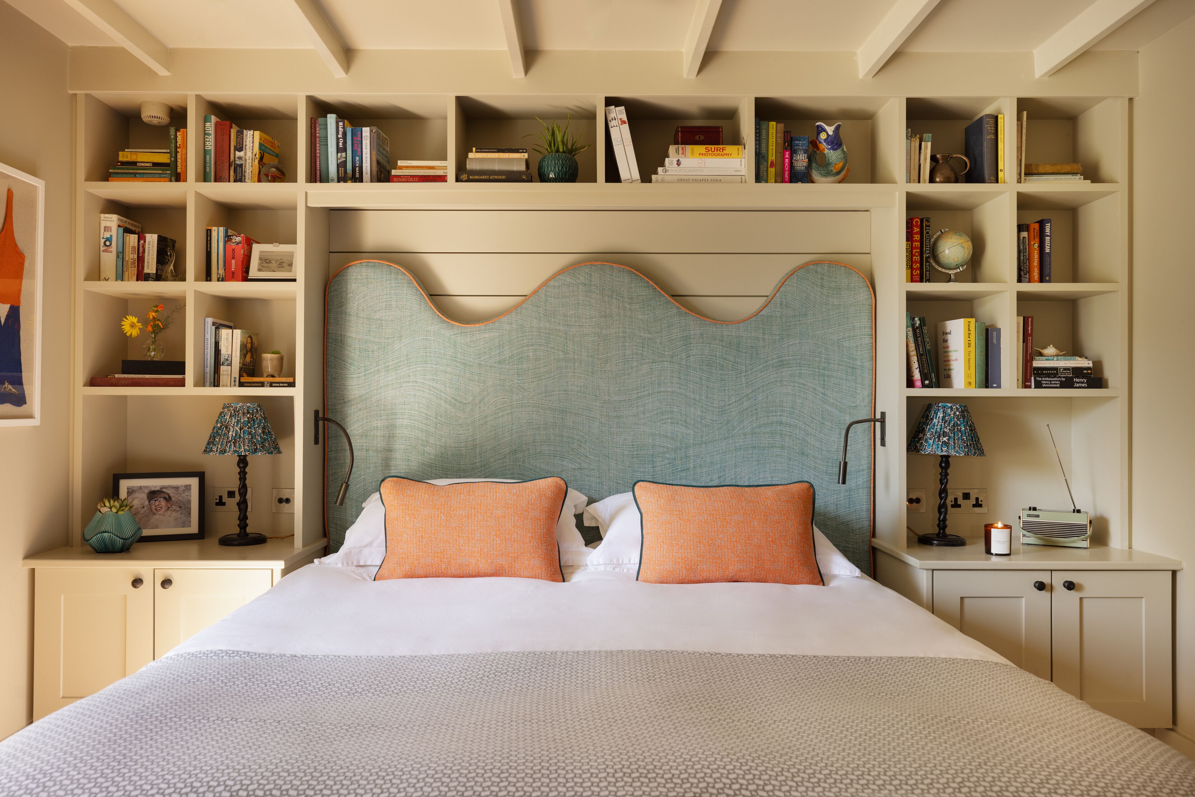 A neatly arranged bedroom with a large bed, two nightstands, a bookshelf, and a decorative headboard.