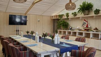A conference room with a long table, chairs, a flat-screen TV, and shelves with plants and decorative items.