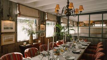 A long dining table set with candles, glassware, and floral centerpieces in a room with striped chairs, a chandelier, and large windows.