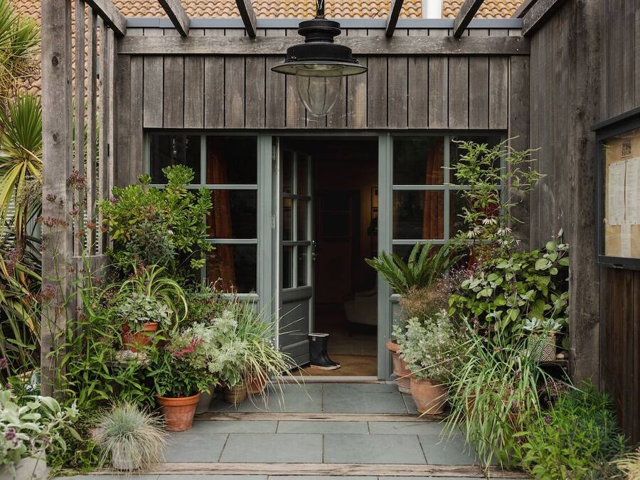 Un bâtiment en bois doté d’une entrée abritée, de plantes en pot et d’un luminaire suspendu.