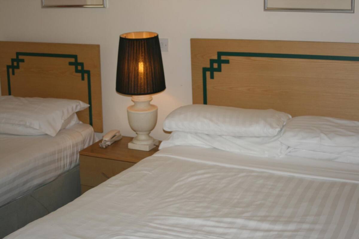 Et hotelværelse med to senge, et natbord med en lampe og en telefon.