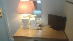 Une petite table de chevet en bois, avec une lampe, une tasse et un plateau contenant une tasse et une soucoupe.