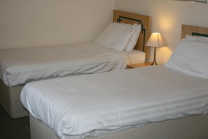 A hotel room with two single beds, a nightstand with a lamp, and a headboard with a wooden panel. - The Hanover Hotel (Liverpool)