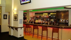 Un espace bar avec un téléviseur fixé au-dessus du comptoir, un menu affiché au mur et plusieurs chaises devant le bar.