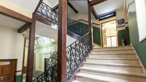 Una escalera con barandillas de metal negro ornamentadas y peldaños color beige, que conduce a una habitación con la señalización "Hostal Castilla II".