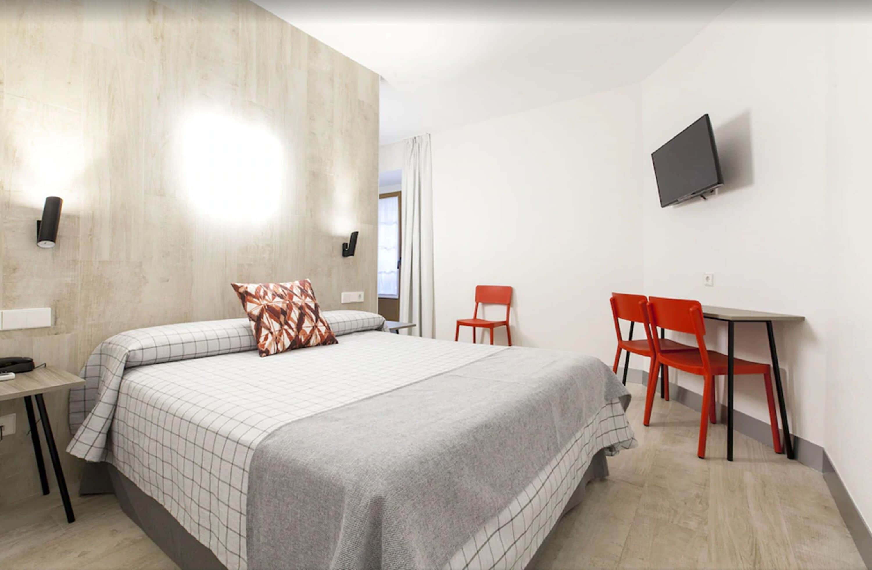 Een moderne hotelkamer met een groot bed, een bureau, twee rode stoelen en een flatscreen televisie aan de muur.