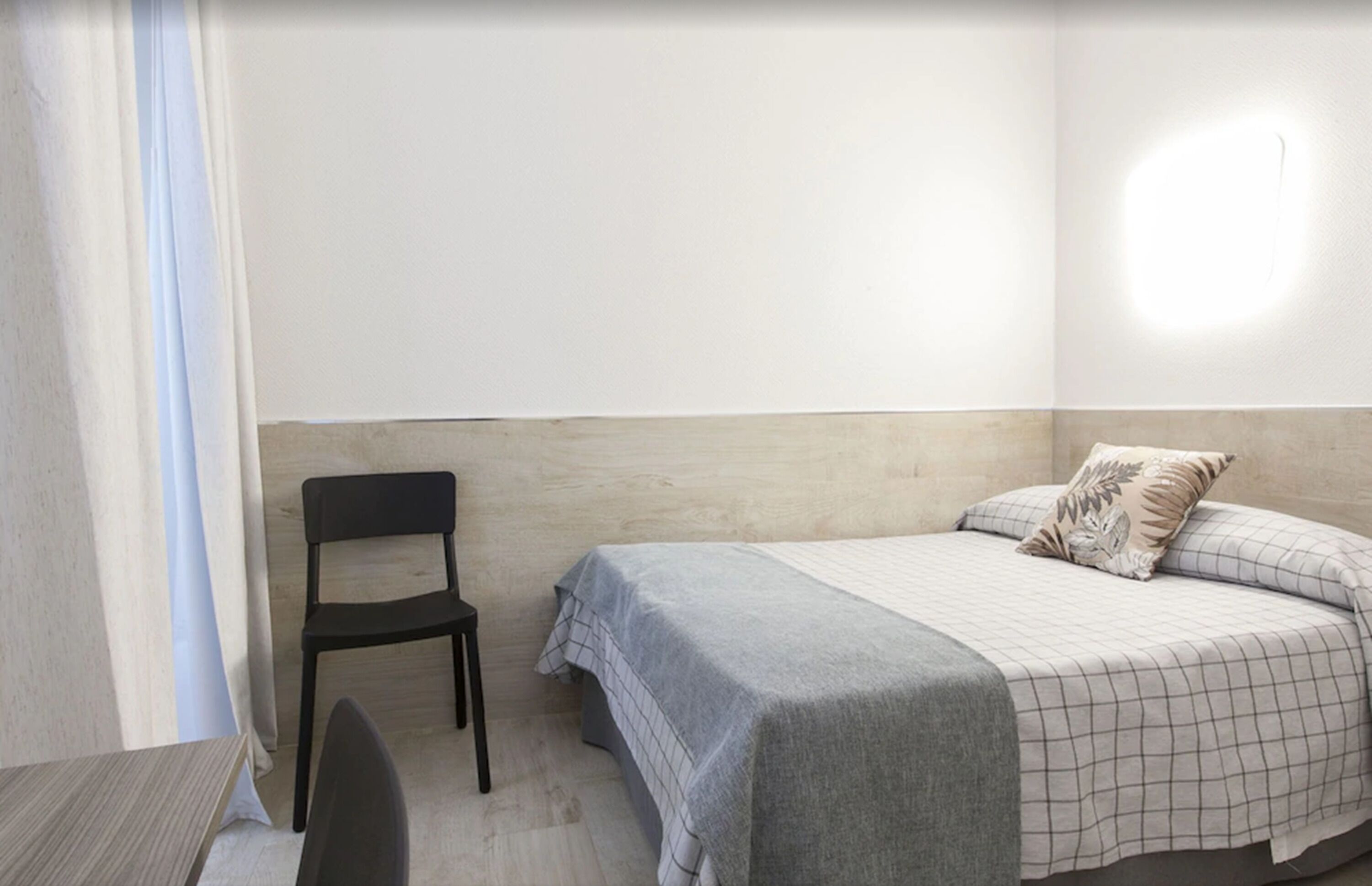 Una habitación pequeña y sencilla con cama, una silla y una mesa.