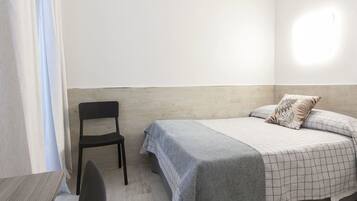 Una habitación pequeña y sencilla con cama, una silla y una mesa.