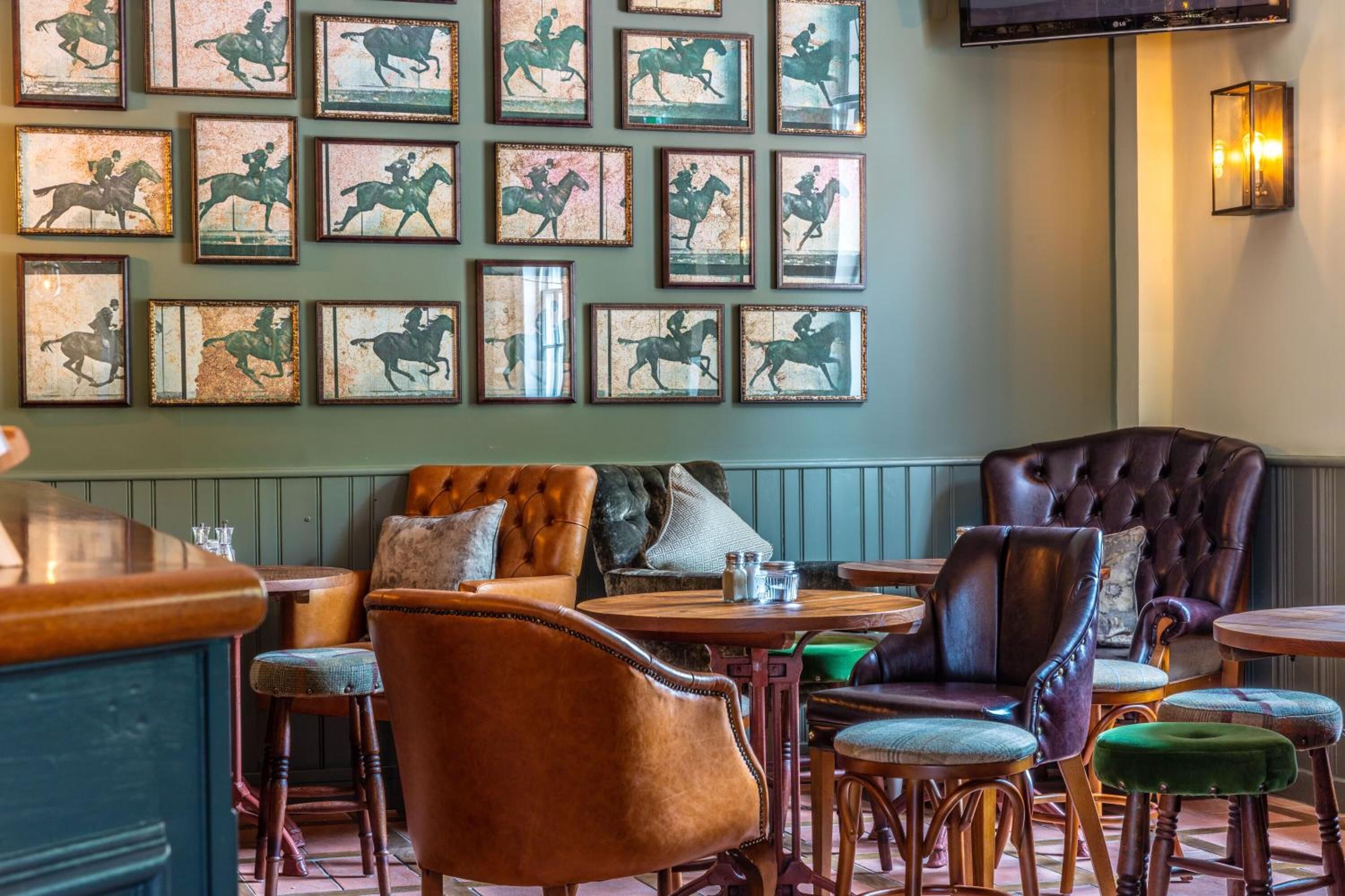 A restaurant with a wall of framed horse racing images, leather seating, and a bar area.