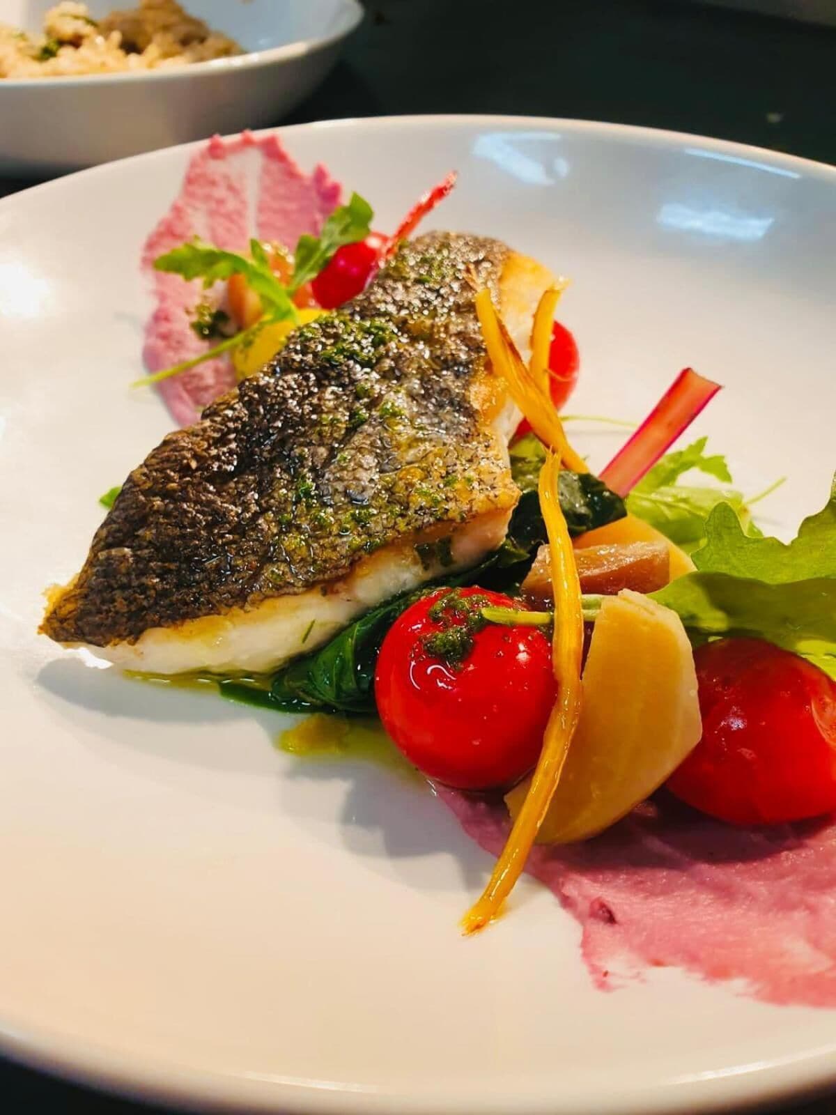 Un plato con un filete de pescado, tomates cherry y vegetales verdes.