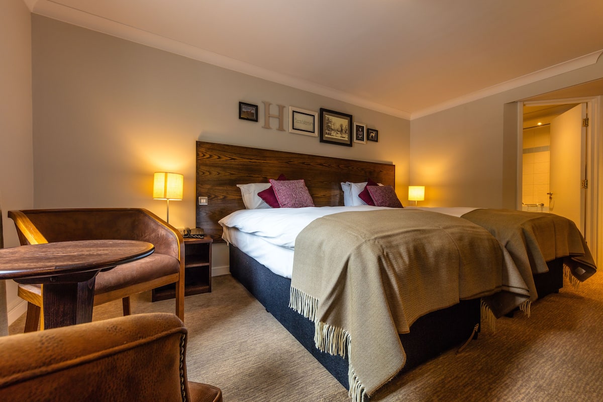 Une chambre d’hôtel avec un lit, deux tables de chevet, une chaise et une petite table.