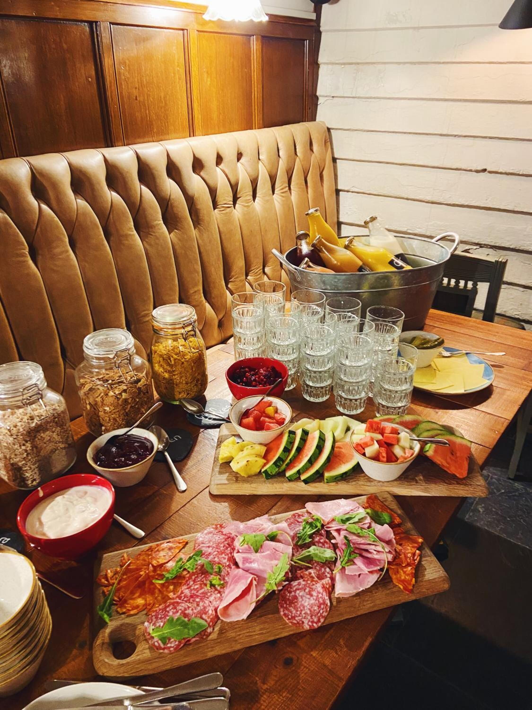 Une table à manger garnie d’une variété d’aliments, notamment des fruits, des fromages et des viandes, ainsi que de plusieurs verres et un seau rempli de boissons.