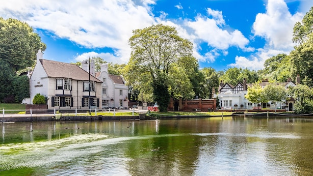 A historic building with a large tree in front, situated beside a calm water body.