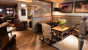 A cozy pub with leather seating, a wooden table with a vase, and framed dog pictures on the wall.