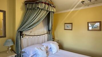 A bedroom with a canopy bed, a bedside table with a lamp, and two framed pictures on the wall.