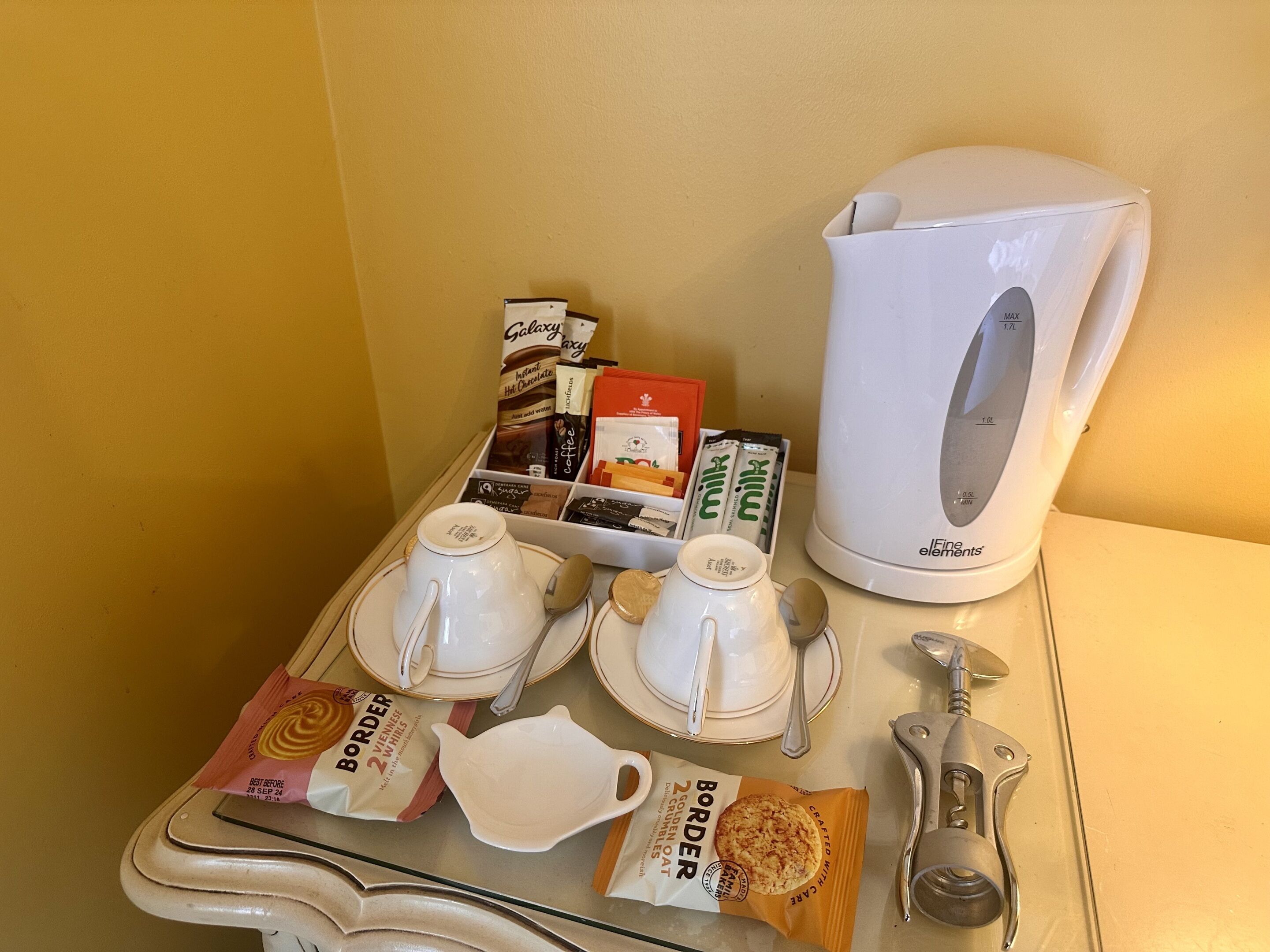 Ein Tisch mit einer weißen Kaffeemaschine, Zuckerportionen, Sahne, Kaffeekapseln und einem Sahnezucker.