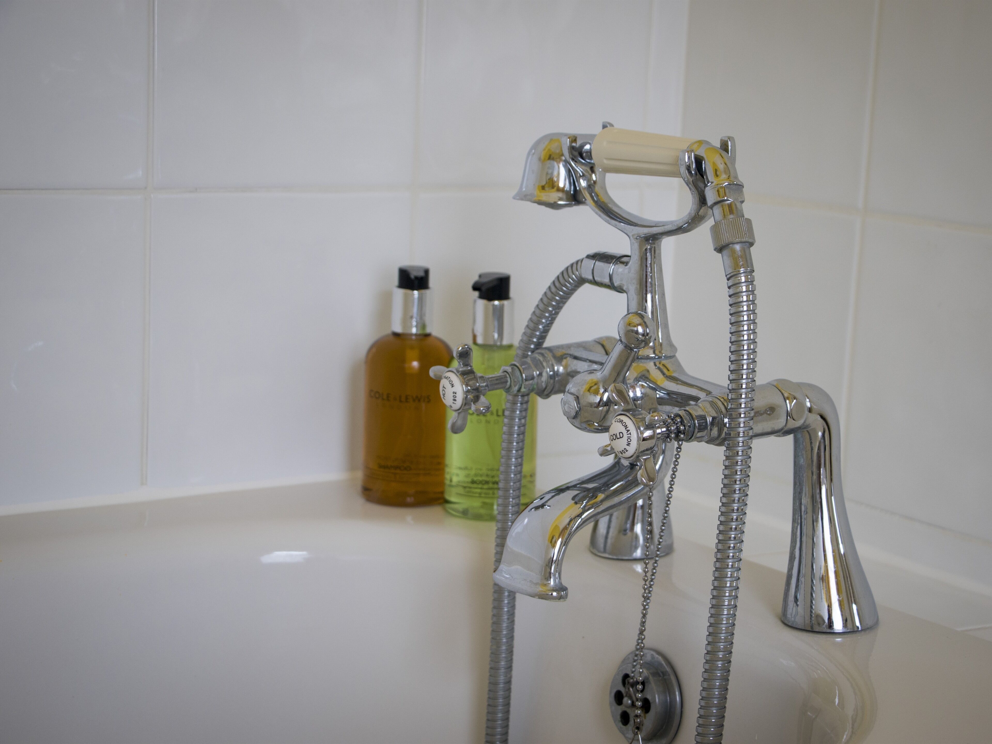 Un baño con un grifo de cromo, un cabezal de ducha y dos botellas de jabón líquido.