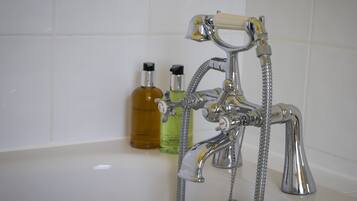 Un baño con un grifo de cromo, un cabezal de ducha y dos botellas de jabón líquido.